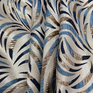 Shiny jacquard fabric in denim blue, navy and gold featuring a raised abstract leaf pattern with shimmering metallic details.